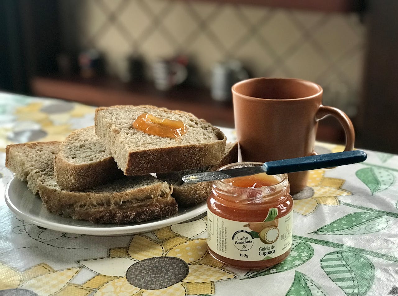 Rustic breakfast setting with sliced bread topped with cupuaçu jam, accompanied by a ceramic mug.