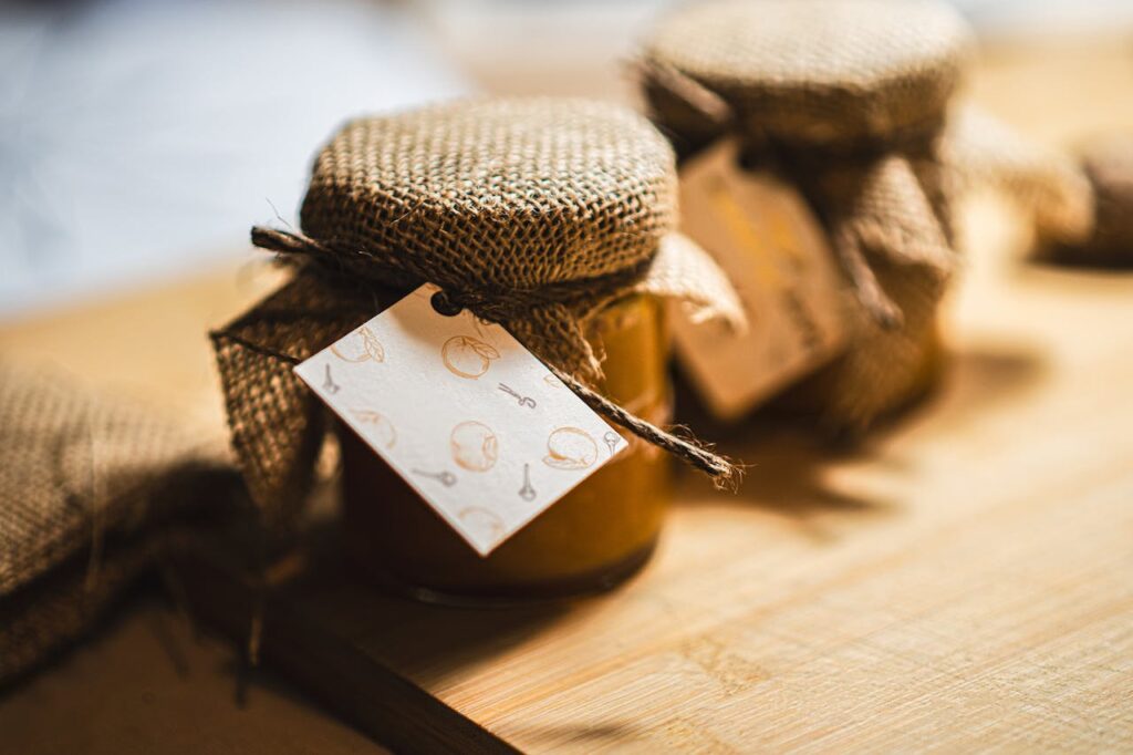 Close-up of burlap-wrapped homemade jam jars on wooden table with labels.