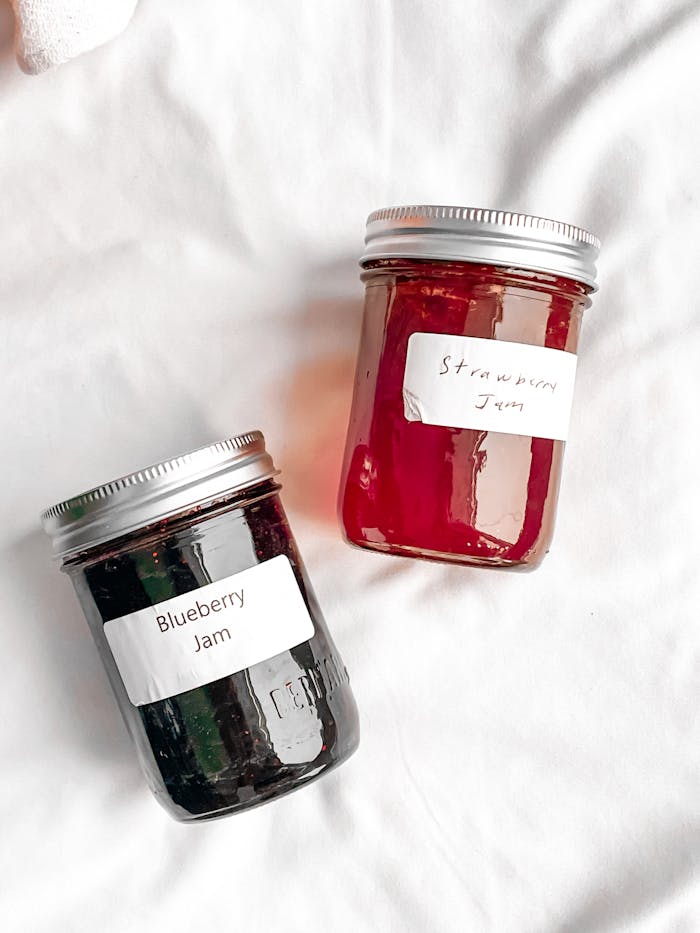 Two jars of homemade blueberry and strawberry jam on a white surface.