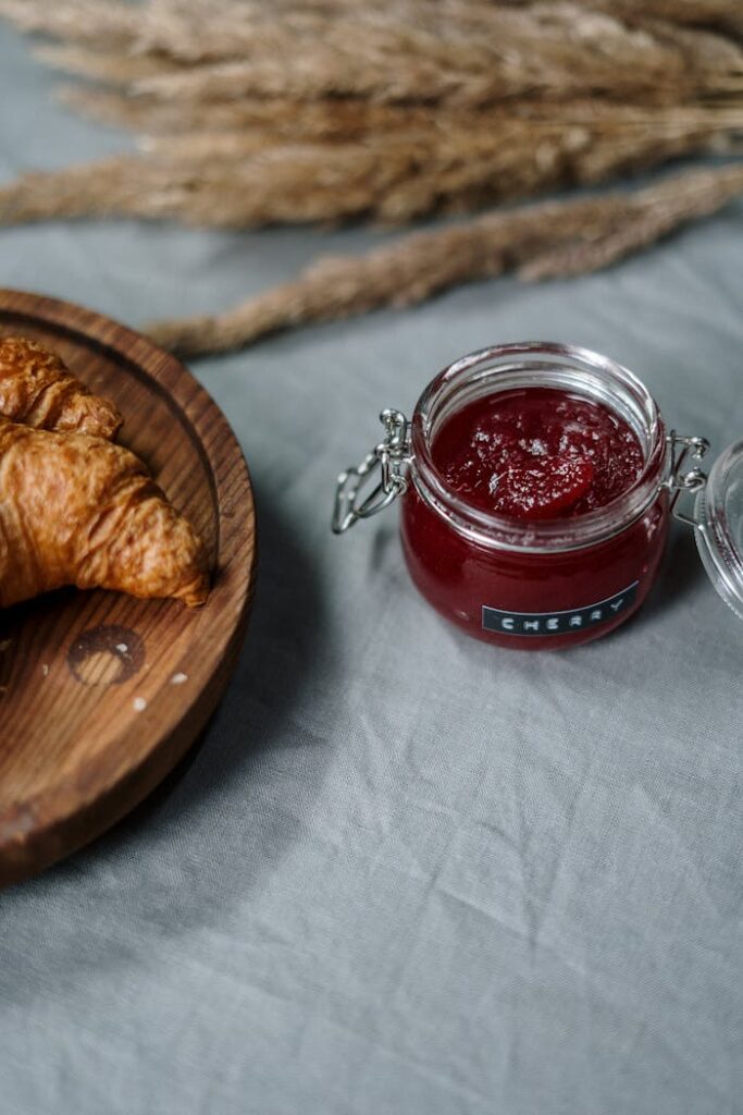 A rustic breakfast scene featuring buttery croissants and a jar of cherry jam.