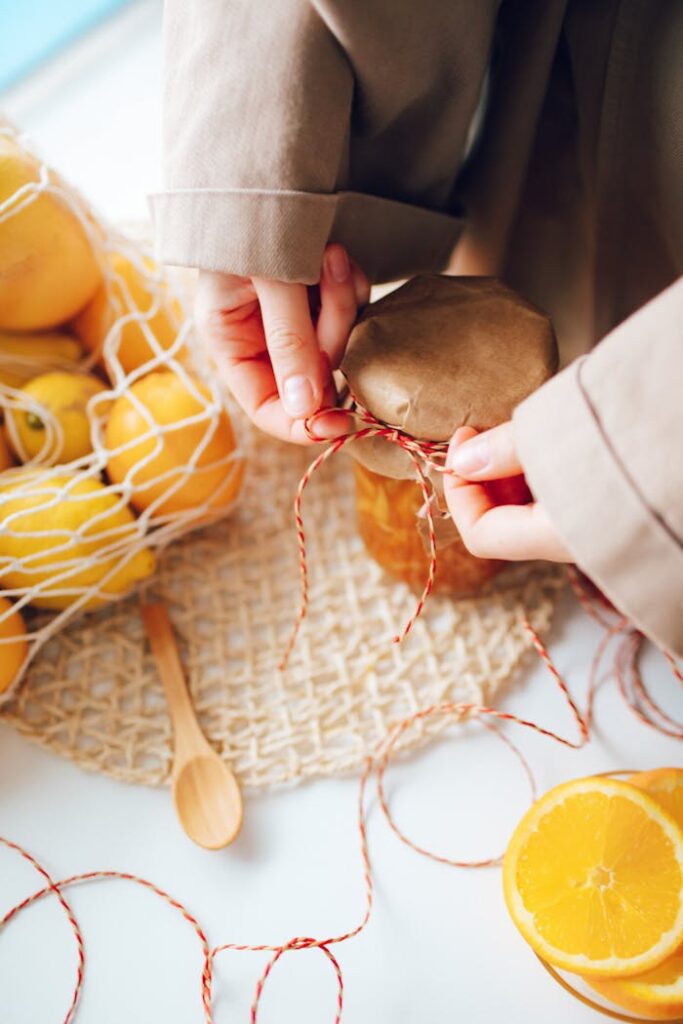 Close-up of hands tying a jar of homemade orange jam next to fresh oranges.