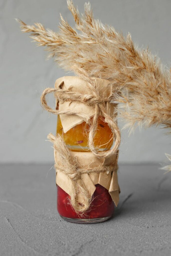 Stacked jars of homemade jams wrapped in rustic paper and twine, accented by dried grasses.
